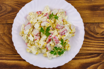 Salad with crab sticks, sweet corn, chinese cabbage, eggs and mayonnaise on wooden table