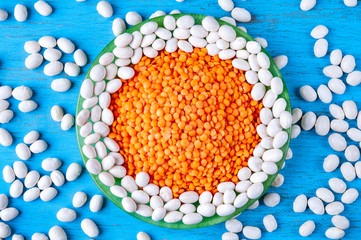 Top view red lentils and white beans in a green plate on a blue wooden background.