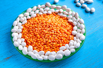 Red lentils and white beans in a green plate on a blue wooden background.