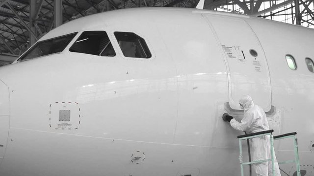 Engineer repairs the door of a passenger plane. The plane in the hangar, door repair. Aviation. Production of passenger Airliners. 4K