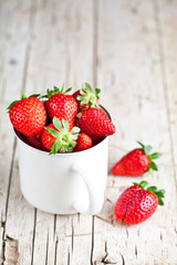 Organic red strawberries in white ceramic cup on rustic wooden background.