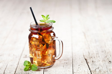 Traditional iced tea with lemon, mint leaves and ice cubes in glass jar on rustic wooden table background.
