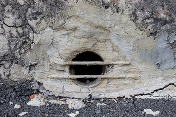 basement window at the bottom of the house with a metal grill and concrete wall
