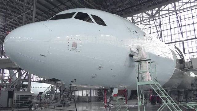 Engineer repairs the door of a passenger plane. The plane in the hangar, door repair. Aviation. Production of passenger Airliners. 4K