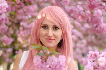 Fototapeta premium Spring beauty girl with pink hair outdoors. Blooming trees. Romantic young woman portrait. Nature
