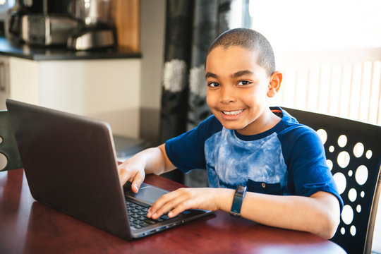 Black boy sitting playing on a laptop computer at home