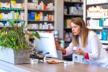 Poster de jardin Pharmacie Pharmacien faisant un dossier de prescription par ordinateur en pharmacie. Portrait d& 39 une pharmacienne travaillant avec un ordinateur derrière un comptoir en pharmacie