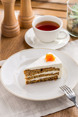 Slice of carrot cake with cream cheese frosting and cup of tea on wooden table