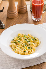 Conchiglie pasta with herbs and glass of tomato juice on wooden table