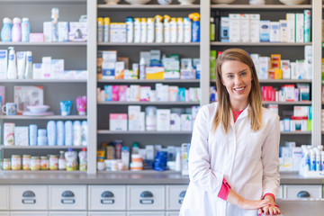 Medicine, pharmaceutics, healthcare and people concept. Portrait of a happy female pharmacist. Cheerful pharmacist chemist woman standing in pharmacy drugstore