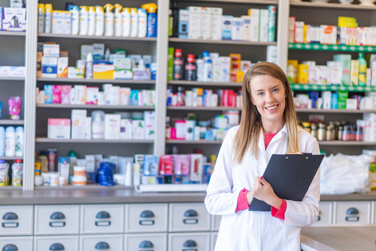 Smiling female pharmacist working in chemist shop or pharmacy. Female happy pharmacist chemist woman standing in pharmacy drugstore