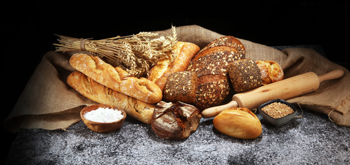 Assortment of baked bread and bread rolls on rustic grey bakery table background