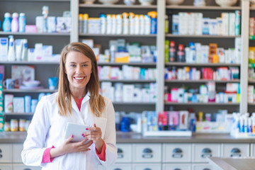 Smiling pharmacist chemist woman standing in pharmacy drugstore, looking at camera. Medicine, pharmacy, people, health care and pharmacology concept - happy young woman pharmacist over drugstore