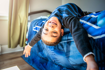 A Cute portrait of child upside down, lying on bed, smiling at camera and playing with toy