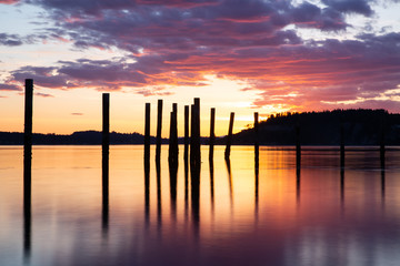 old pilings reflected in water with dramatic sunrise