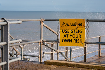 A danger sign at a british coastline with waves crashing in the background.