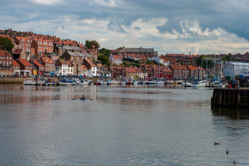 Fototapeta na wymiar Whitby Harbour on a hot summers day with dark clouds and an islotaed rowing boat on the water.