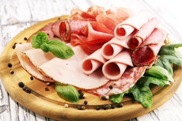 Food tray with delicious salami, pieces of sliced ham, sausages,salad and vegetable. Meat platter with selection