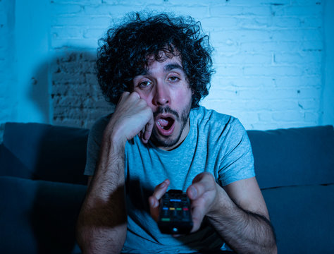 Lifestyle Portrait Of Young Millennial Man Watching Boring Tv Feeling Sleepy At Night