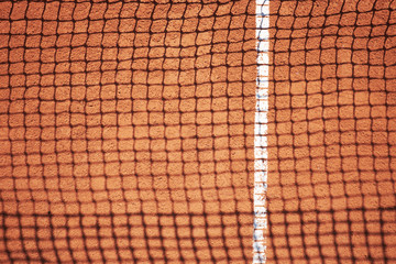 Shadow of tennis net on red sand field