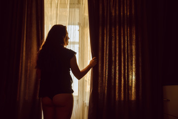 young sexy woman in panties opening curtains in the morning