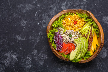 Fototapeta na wymiar Buddha bowl with chickpea, avocado, wild rice, quinoa seeds, bell pepper, tomatoes, greens, cabbage, lettuce on dark stone table. Vegetarian super food. Top view with copy space.