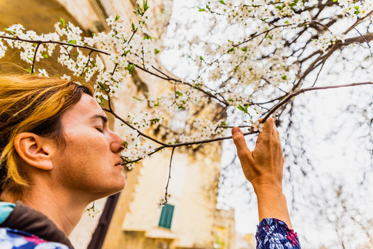 Mature Real Woman Smelling The Flowers Of A Tree In Spring.