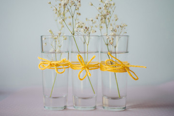 floral decoration: three small glass vases with white flowers; gypsophila on a blue background; yellow canvas bows