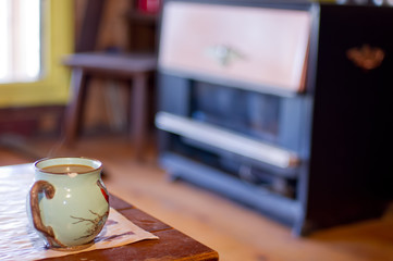 Steaming cup of coffee in bird mug with a vintage propane / natural gas cabin heater in the background - taken at a rustic cabin in Northern Wisconsin