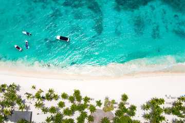 Aerial view from drone on caribbean island with coconut palm trees, sunbeds and boats floating in the sea