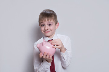 Fototapeta na wymiar Happy boy puts a coin in a pink piggy bank. Business concept. Light background