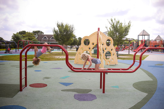 two girls climbing on playground monkey bars upside down