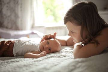 older sister gently touches newborn baby on bed