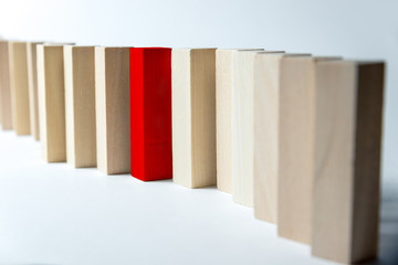 A long curved line of wooden cubes with one red, as a symbol of a queue, competition for a position or team, on a uneven white background. Horizontal frame