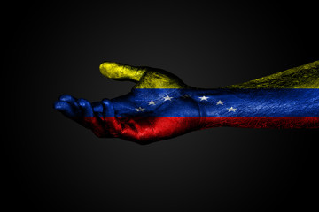 Fototapeta premium An outstretched hand with a painted flag of Venezuela, a help sign or a request, on a dark background.