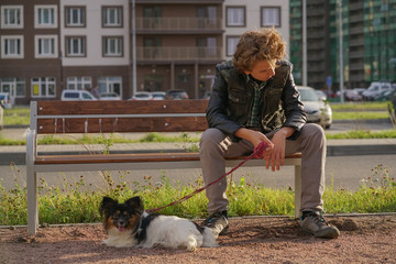 sad lonely guy sitting on a bench with his dog. the difficulties of adolescence in communication...