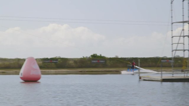 Wide panning shot of a man enjoying smooth cable water skiing at a calm water sports location, GC Wake Park, Australia