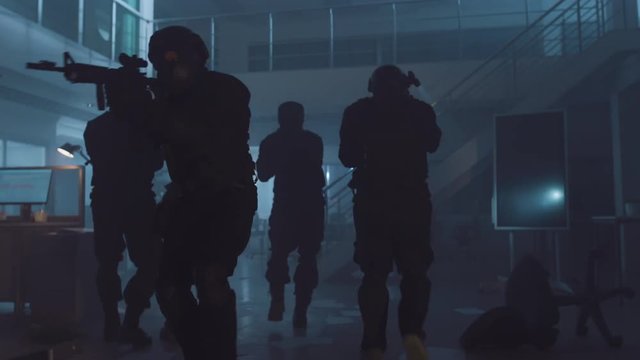 Masked Team of Armed SWAT Police Officers Slowly Move in a Hall of a Dark Seized Office Building with Desks and Computers. Soldiers with Rifles and Flashlights Surveil and Cover Surroundings.