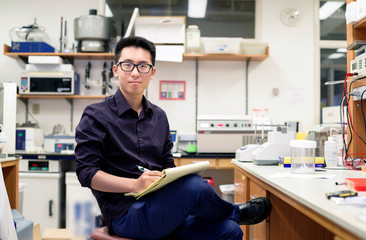 Asian man writing on notepad in electronics workshop