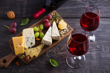 Glass and bottle of wine with cheese, grapes, and nuts on black wooden table. Wine and food. View from above, top studio shot