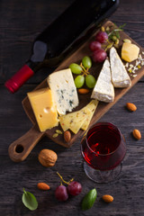 Glass and bottle of wine with cheese, grapes, and nuts on black wooden table. Wine and food. View from above, top studio shot