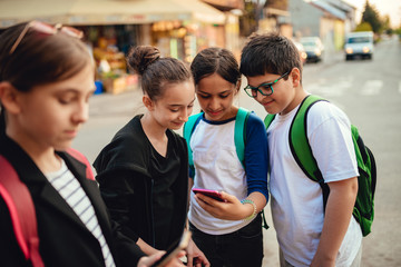 Group of school children using phone on the street