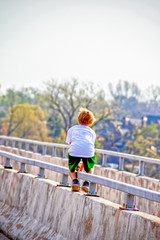 Little boy - unrecognizable- climbing on bridge over river pausing to look out over wooded residential area - blurred bokeh background and motion blur