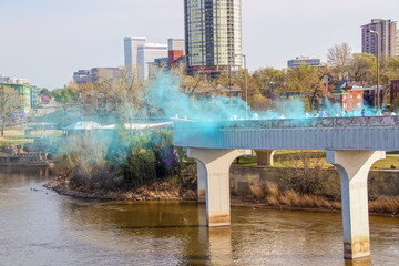 The blue powder station on a bridge over the Arkansas River at a color holi festival in Tulsa USA with people running through in the distance and the city skyline behind