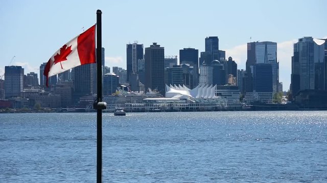 The ordinary Vancouver downtown view from Lonsdale quay North Vancouver. The Canadian flag waving in the sky.The seabuses are on the sea.