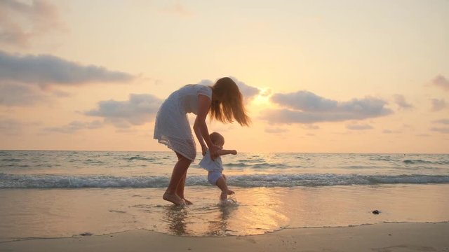 YounYoung Beautiful Woman Walks With Her Little baby On The Seashore At Sunsetg Beautiful Woman Walks With Her Little baby On The Seashore At Sunset. 4k