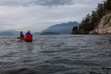 Couple adventurous female friends on a red canoe are paddling in the Howe Sound during a cloudy sunset. Taken in Horseshoe Bay, West Vancouver, BC, Canada.