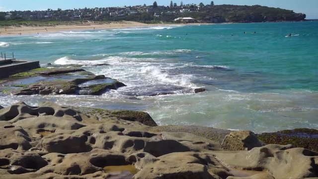 4k Video -Waves crashing on the rocks at South Curl Curl Beach near the Rockpool with people in the background enjoying water sports on a beautiful sunny day -Northern Beaches, Sydney, NSW, Australia.