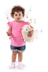 Toddler girl with Easter eggs hugs Easter lamb plush toy, isolated on white