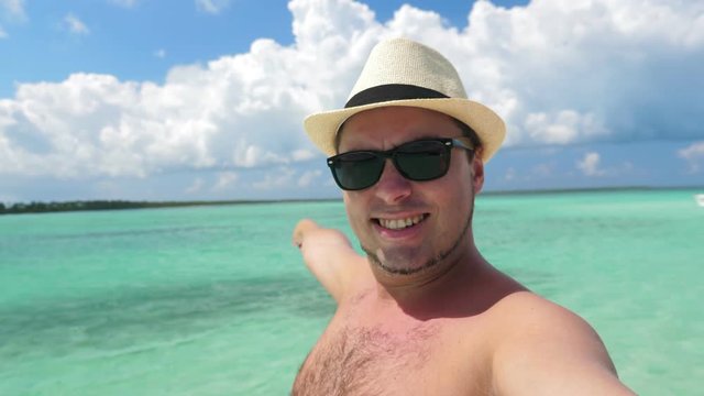 Portrait young man in hat taking selfie video on tropical beach with caribbean sea background. Summer holidays. Travel vacation